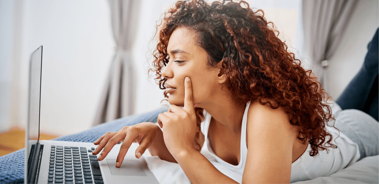 Woman laying down on bed, using laptop, viewing a PPC ad