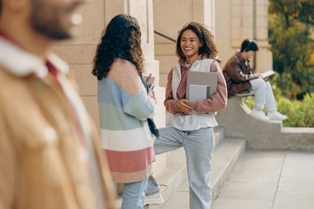 College students talking outside a university building between classes, showcasing campus life and student experience as part of higher education marketing and recruitment efforts.