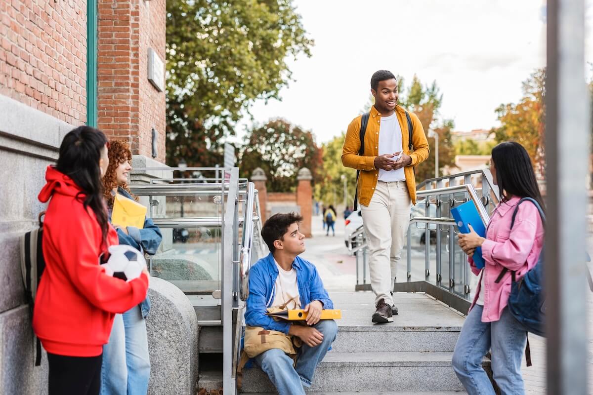Group of students talking outside campus steps, illustrating enrollment marketing for educational institutes.
